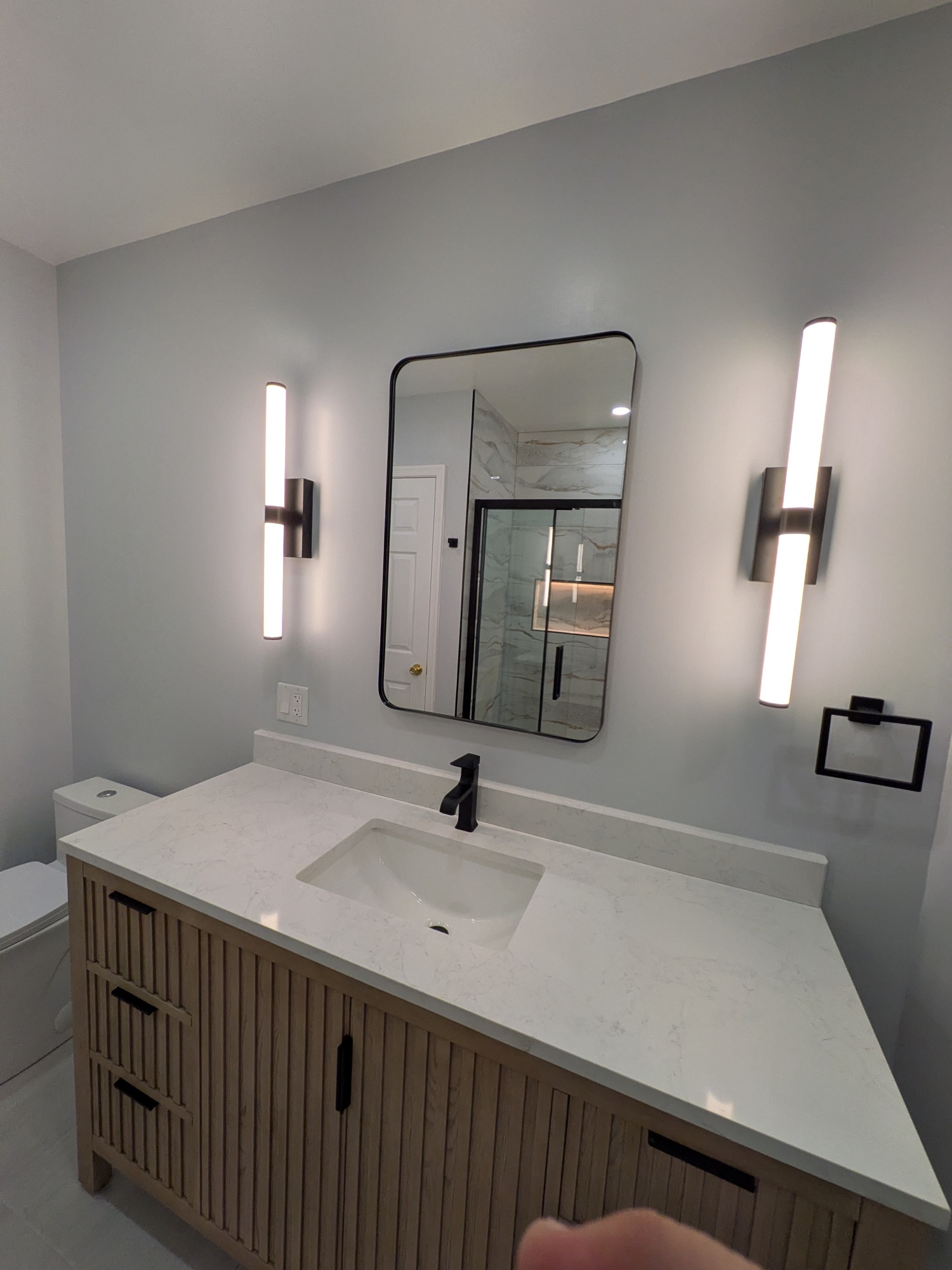 Fluted white-oak vanity with quartz top, framed mirror, and linear sconces